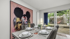 A dining area with a large abstract painting, a modern table set for four, and a view of the backyard through glass doors. - Sunset Townhouse With Free Parking (Brighton)