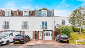 A row of white terraced houses with a small front garden, a white van parked in front, and two cars parked in the driveway. - Sunset Townhouse With Free Parking (Brighton)