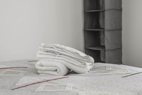Uma pilha de toalhas dobradas sobre um espalha-cama texturizado em um quarto com cabeceira cinza estofada.