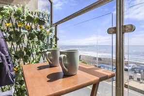 Una mesa de madera con dos tazas grises en un balcón con vista a una playa.