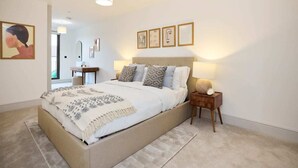 Une chambre à coucher avec un grand lit, des tables de chevet et des œuvres d’art encadrées accrochées au mur.