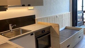 Kompakti keittiö, jossa on sisäänrakennettu uuni, pesuallas ja puinen penkki, joka on integroitu keittiökaapistoon.