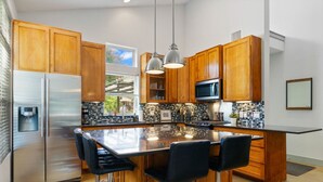 A modern kitchen with wooden cabinets, stainless steel appliances, a large island with bar stools, pendant lighting, and a view of the outdoors. - 2915 E 14th xxxxxxxx (Austin)