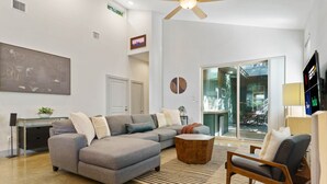 A modern living room with a sectional sofa, a coffee table, and a TV. There is a glass door leading to a balcony. - 2915 E 14th xxxxxxxx (Austin)