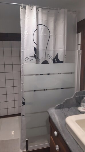A bathroom with a white shower curtain featuring black cat silhouettes, a tiled wall, and a wooden vanity with a sink.