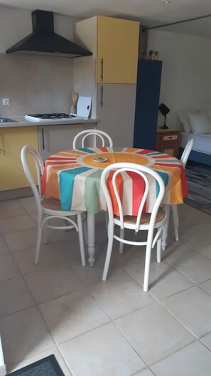 A dining area with a table covered by a colorful tablecloth, surrounded by white chairs.