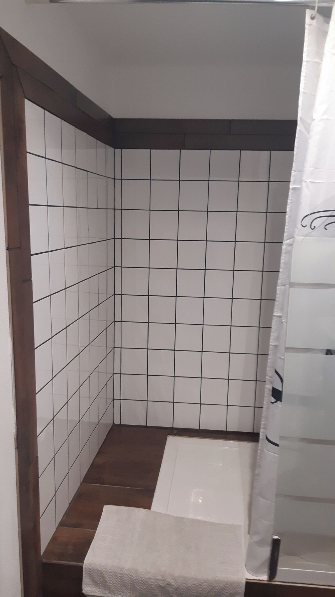 Un baño pequeño con baldosas, cortina de ducha, un banco y piso de madera.