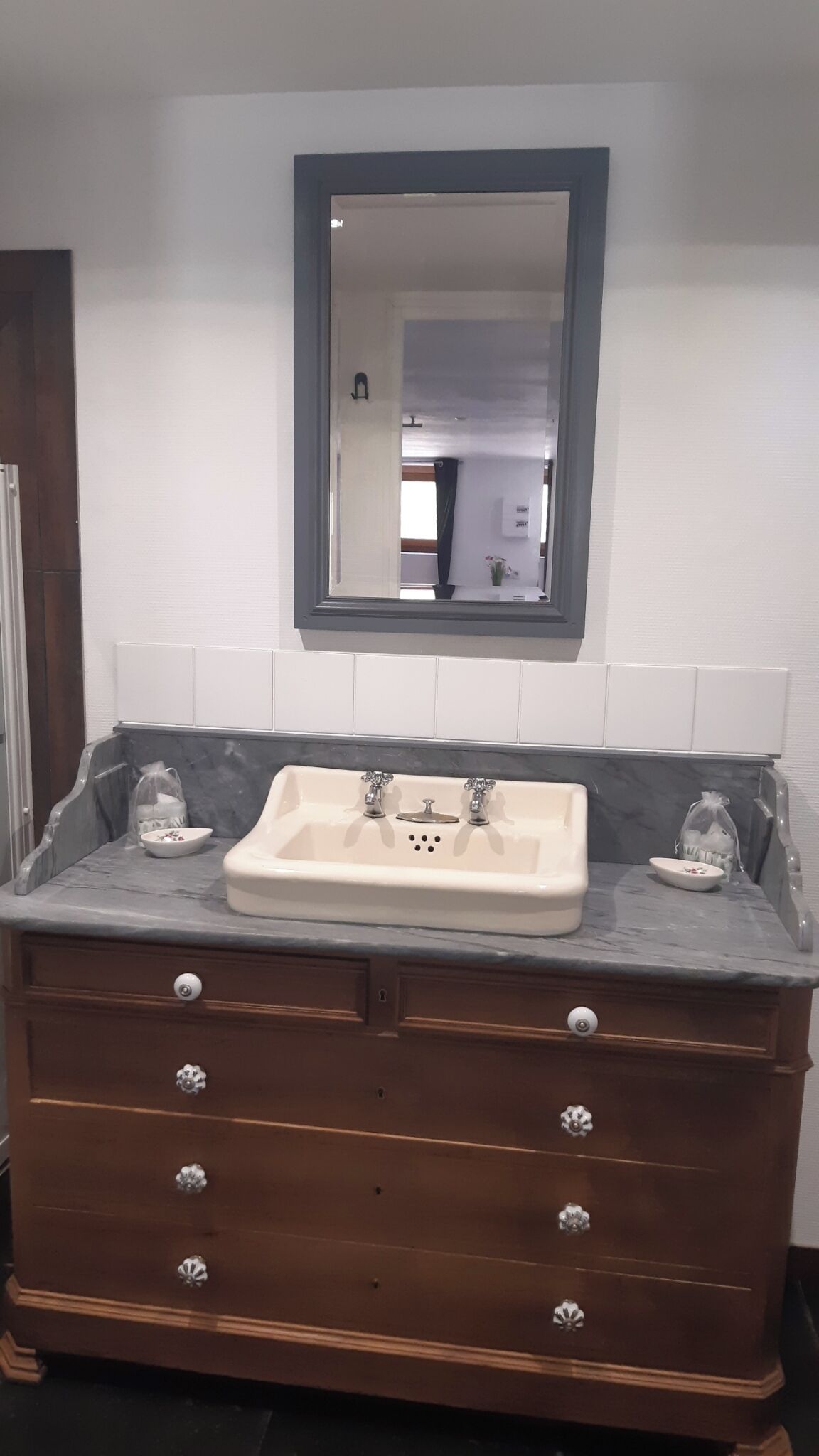 A bathroom with a marble countertop, a sink with two faucets, a mirror above the sink, and a wooden vanity with drawers.