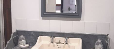A bathroom with a marble countertop, a sink with two faucets, a mirror above the sink, and a wooden vanity with drawers.