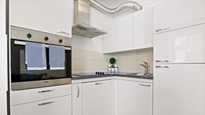 A modern kitchen with white cabinetry, a stainless steel oven, and a built-in range hood. - Charming White Apartment with Balcony and Parking (Rovinj)