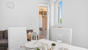 A dining area with a table set for two, a sofa, and a view of the outdoors. - Charming White Apartment with Balcony and Parking (Rovinj)