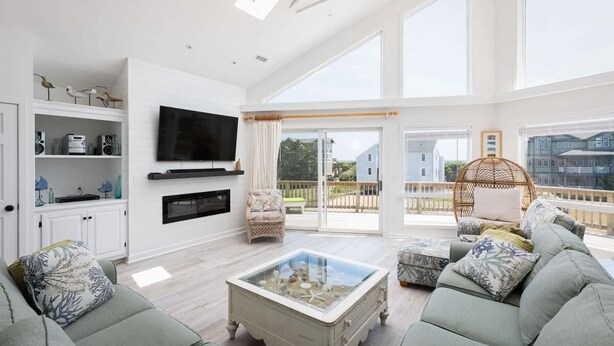 A spacious living room with a large TV, comfortable seating, a glass coffee table, and a balcony with a view. - Private Semi-Oceanfront Retreat with Pool & Spa (Corolla)
