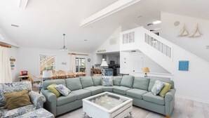A spacious living room with a large sectional sofa, a glass coffee table, and a staircase leading to an upper level. - Private Semi-Oceanfront Retreat with Pool & Spa (Corolla)