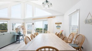 A bright dining room with a large wooden table and chairs, large windows, and a view of the outdoors. - Private Semi-Oceanfront Retreat with Pool & Spa (Corolla)