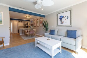 A modern living room with a white sofa, a coffee table, and a dining area with a table and chairs.