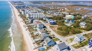 Ovenfra ses et kystnære boligområde med ejendomme direkte ved stranden, herunder huse og et hotel med swimmingpool.