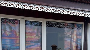 Un edificio con tres ventanas con cortinas decorativas, una puerta blanca y un suelo de hormigón con objetos de colores.