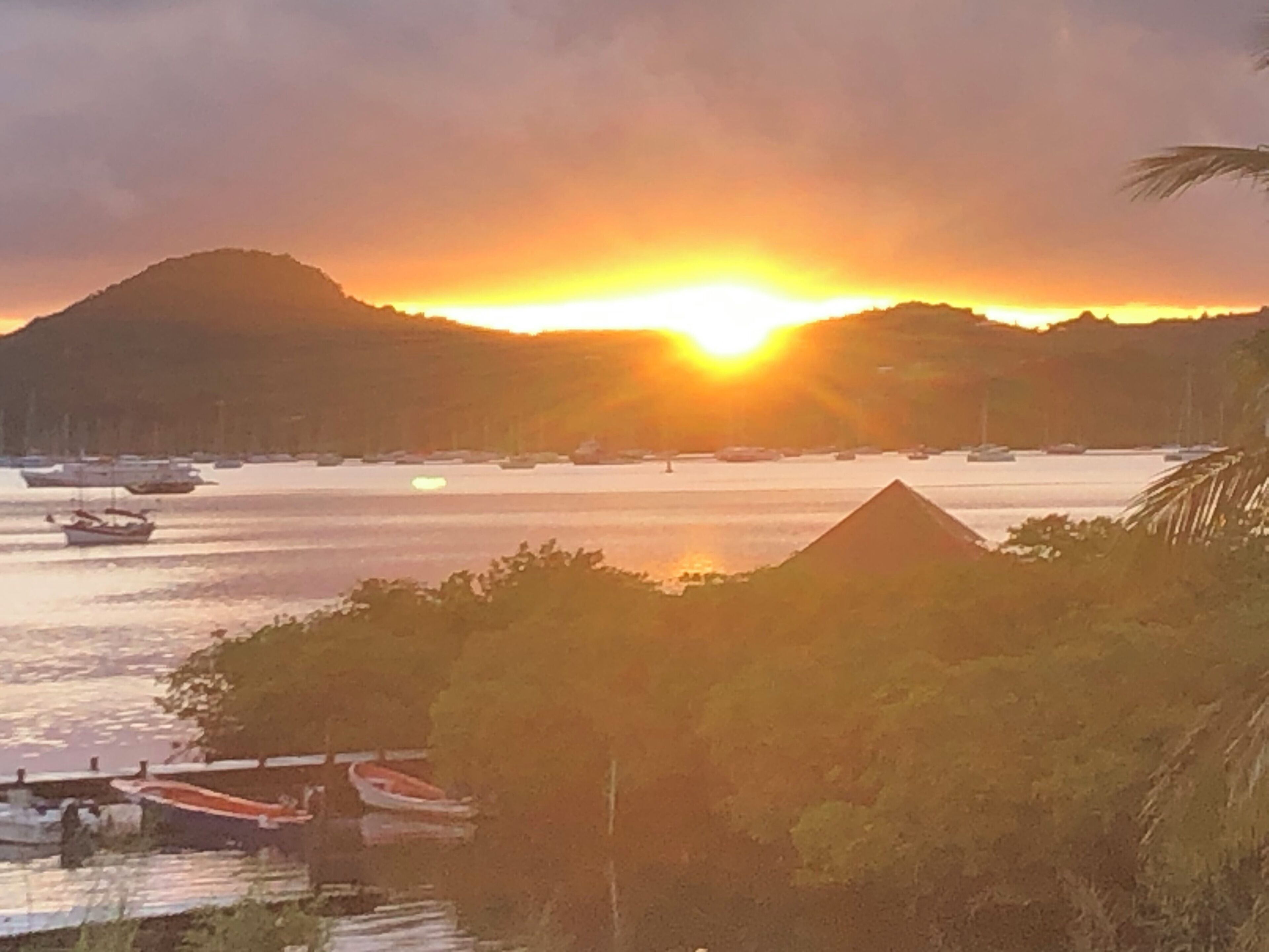 A sunset over a body of water with boats and a mountain in the background.