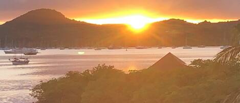 A sunset over a body of water with boats and a mountain in the background.