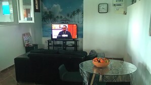 Una sala de estar con televisor, sofá, una mesa de vidrio con fruta y un ventilador de techo.