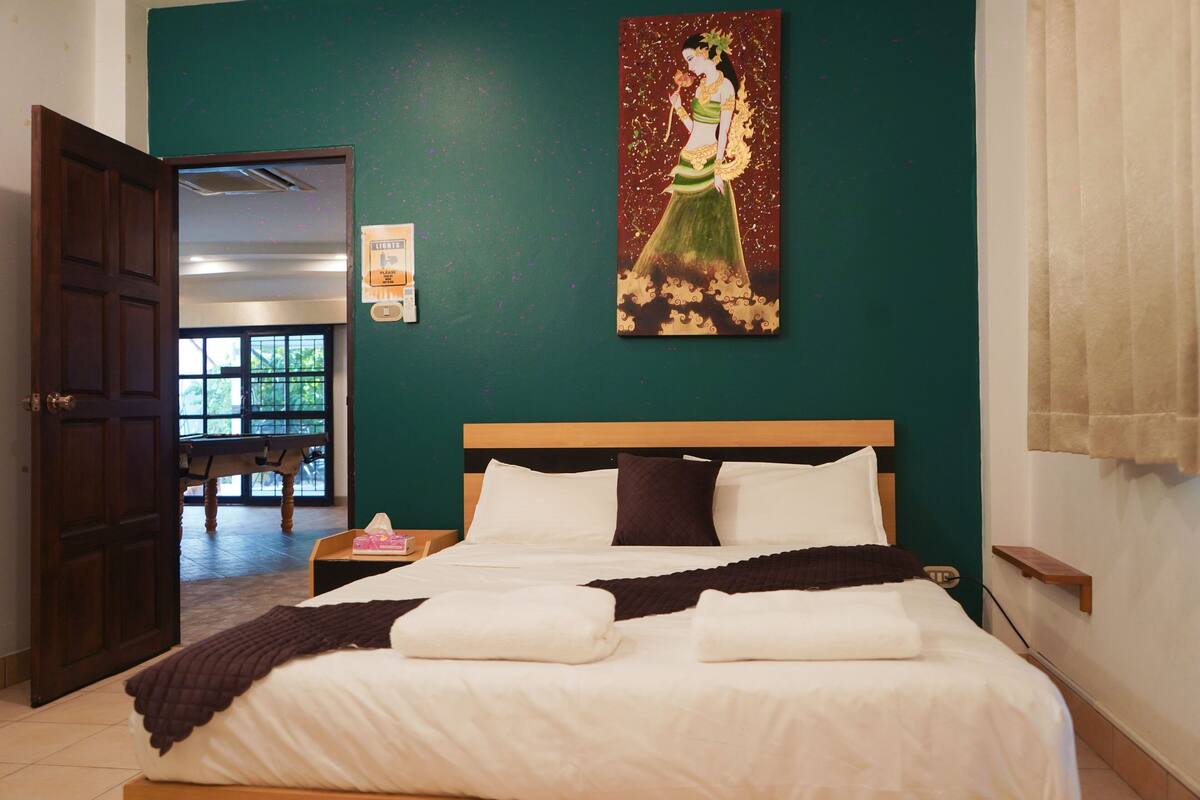 A hotel room with a bed, a painting, a door, and a view of the outside.
