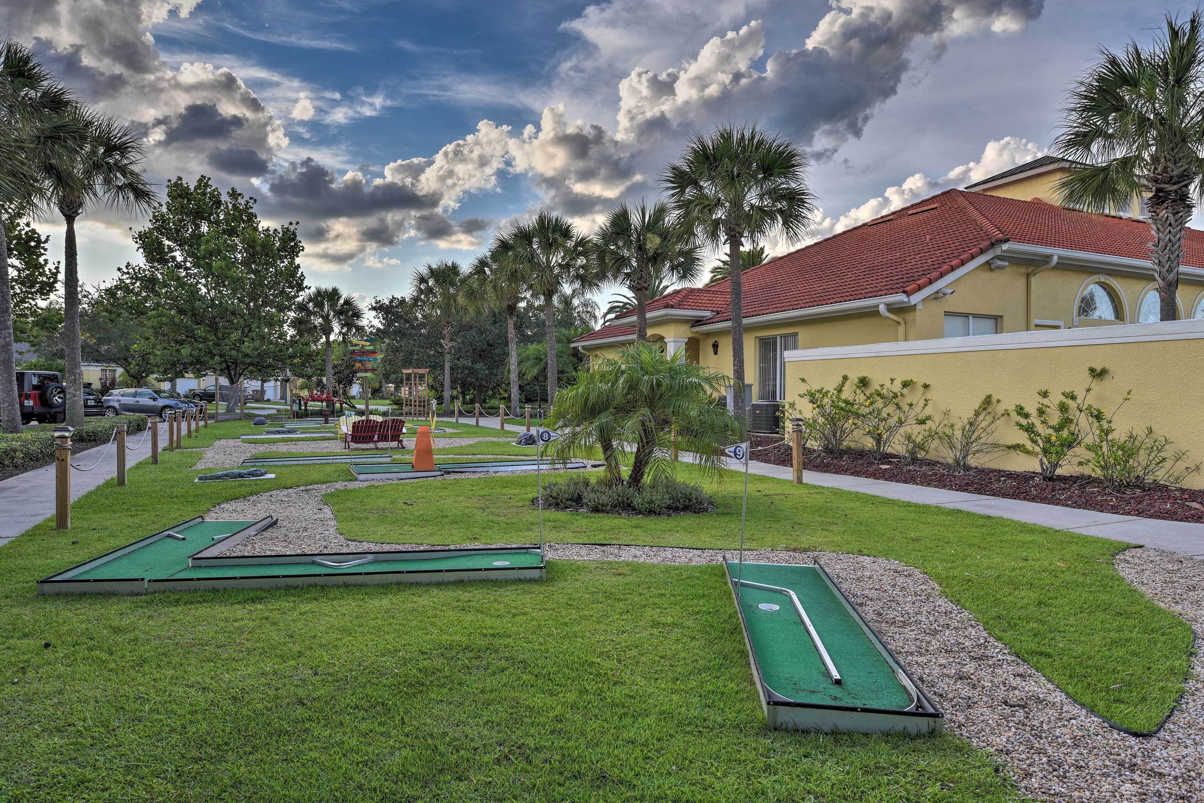 A courtyard with miniature golf holes, palm trees, and a building with a red-tiled roof.