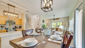 A dining area with a long table set for a meal, a kitchen in the background, and a ceiling fan. - 7 Mi to Disney: Kissimmee Poolside Paradise! (Kissimmee)