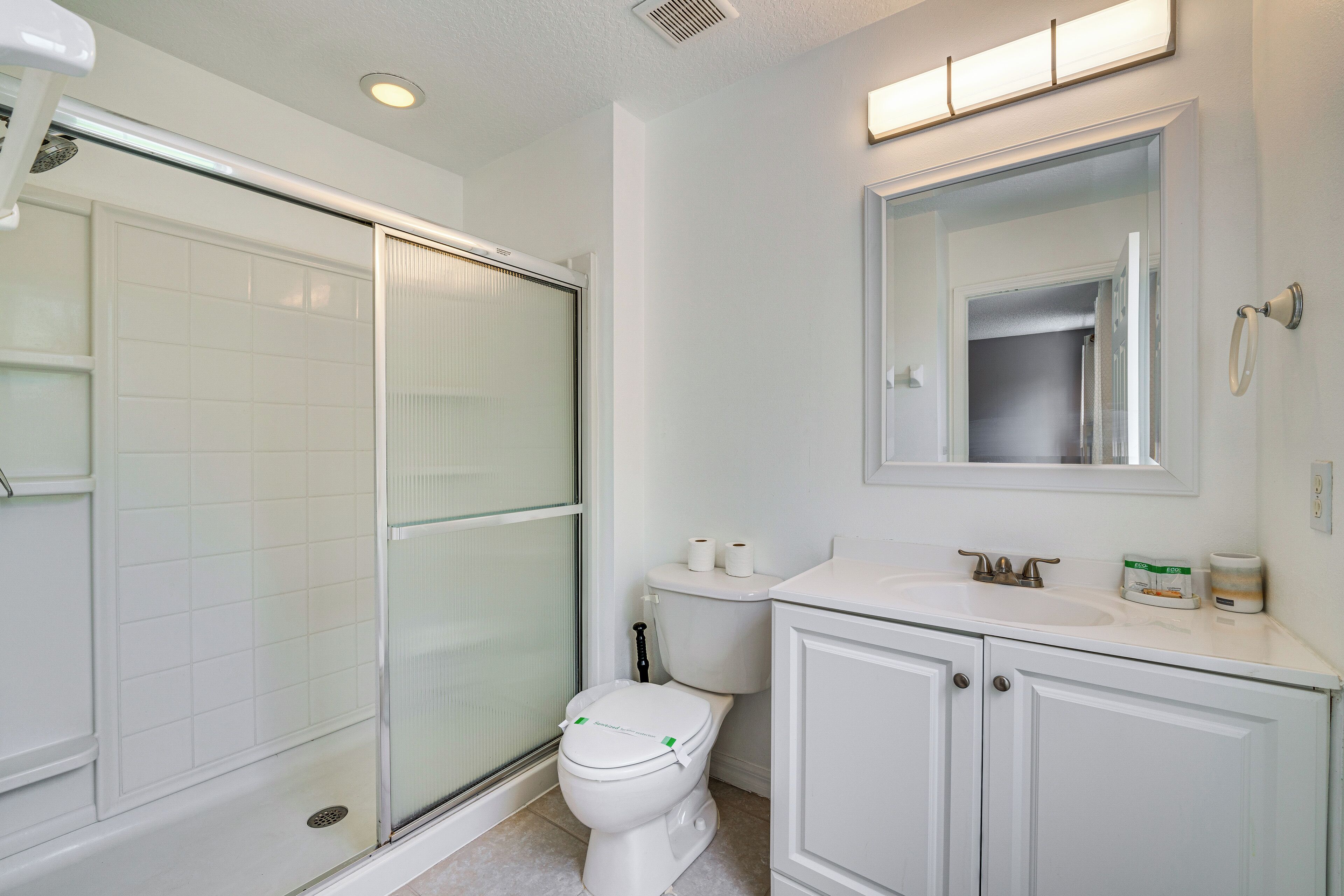 A bathroom with a glass shower enclosure, a toilet, a sink, and a mirror.