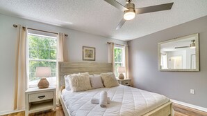 A bedroom with a bed, a nightstand, a ceiling fan, and a window with curtains.