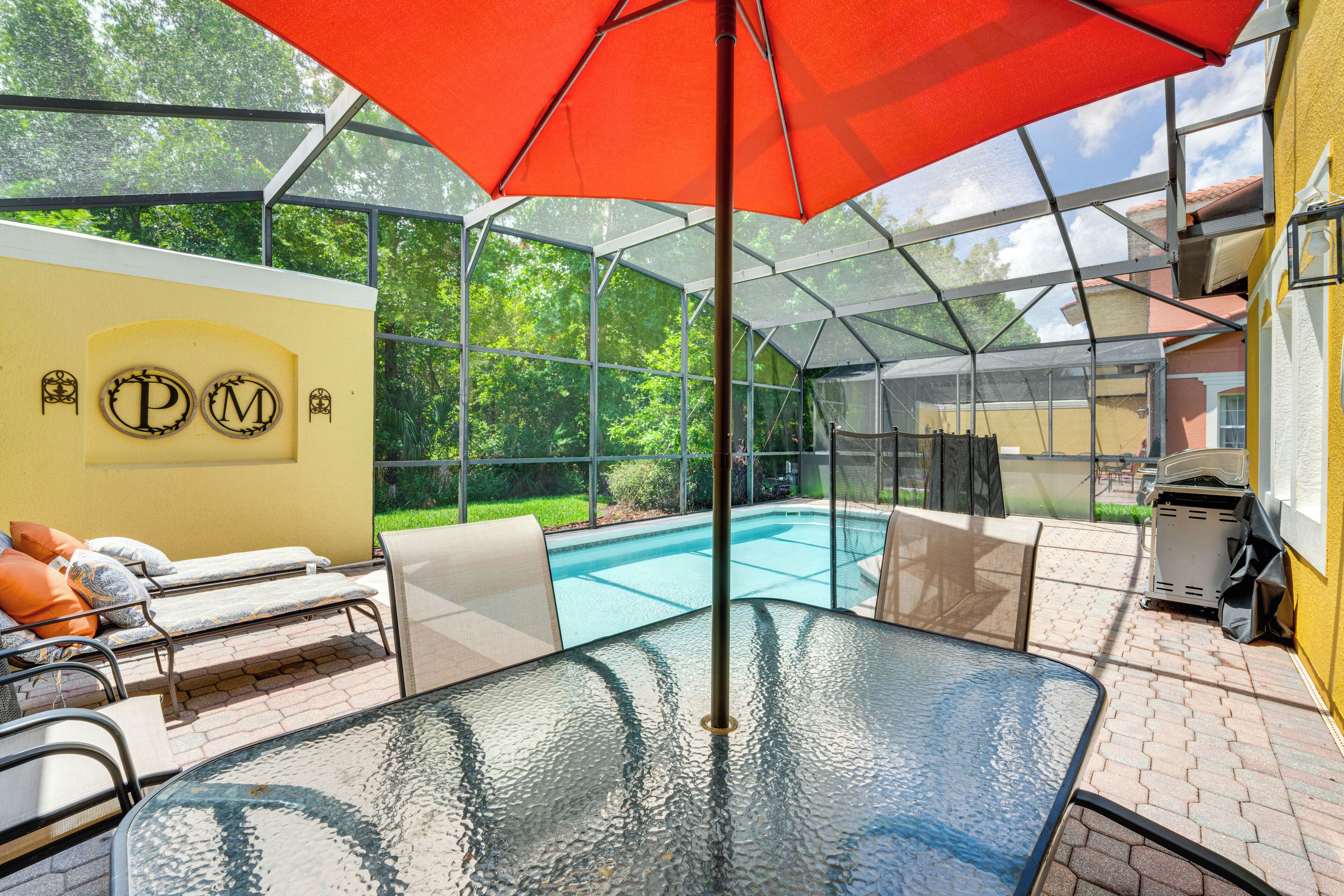 A glass-enclosed patio with a pool, lounge chairs, and a table under a red umbrella.