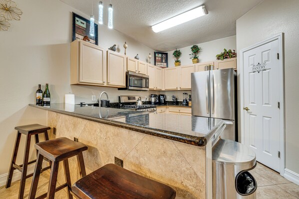 A kitchen with a central island, bar stools, a trash can, and a pantry door. - 14 Mi to Disney: Spacious Home w/ Pool & Lanai! (Davenport)