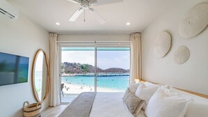 Een slaapkamer met een groot bed, een plafondventilator, een televisie en uitzicht op een strand.
