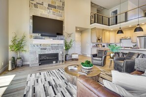 A spacious living area with a stone fireplace, a flat-screen TV, and a modern kitchen with pendant lighting.