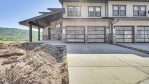 Ein zweistöckiges Haus mit Garage, einer überdachten Terrasse und Blick auf die umliegende Landschaft.