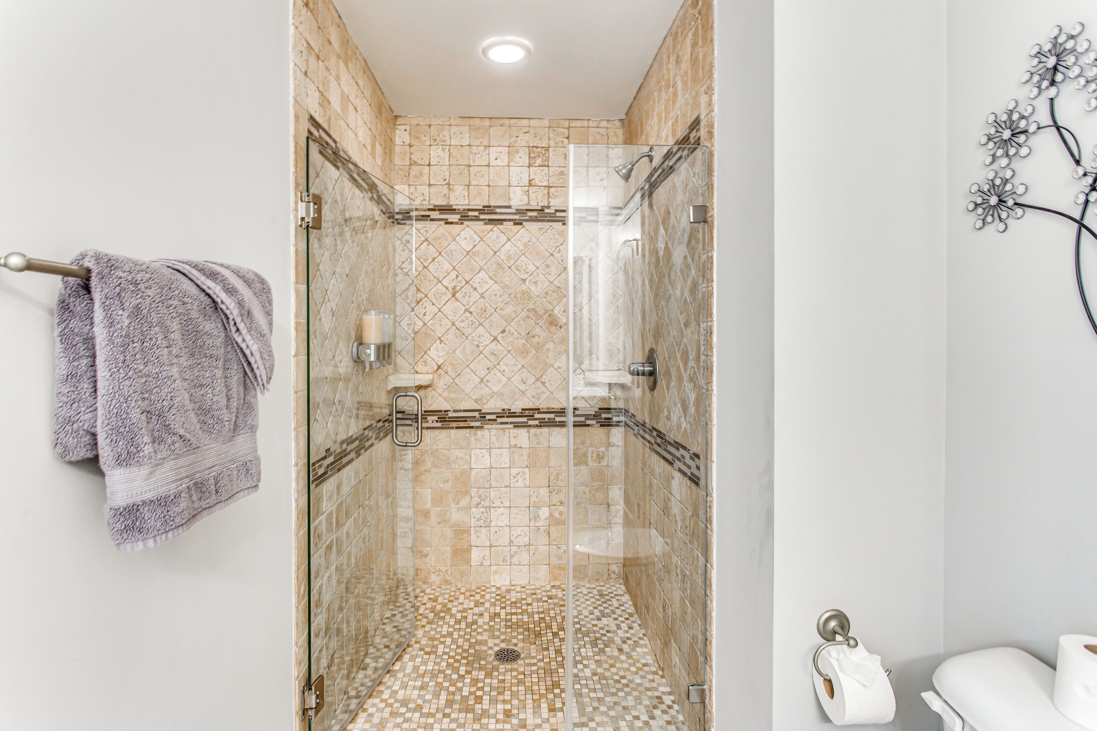 Un baño moderno con ducha de vidrio, paredes con azulejos y un inodoro con soporte para toallas de papel.
