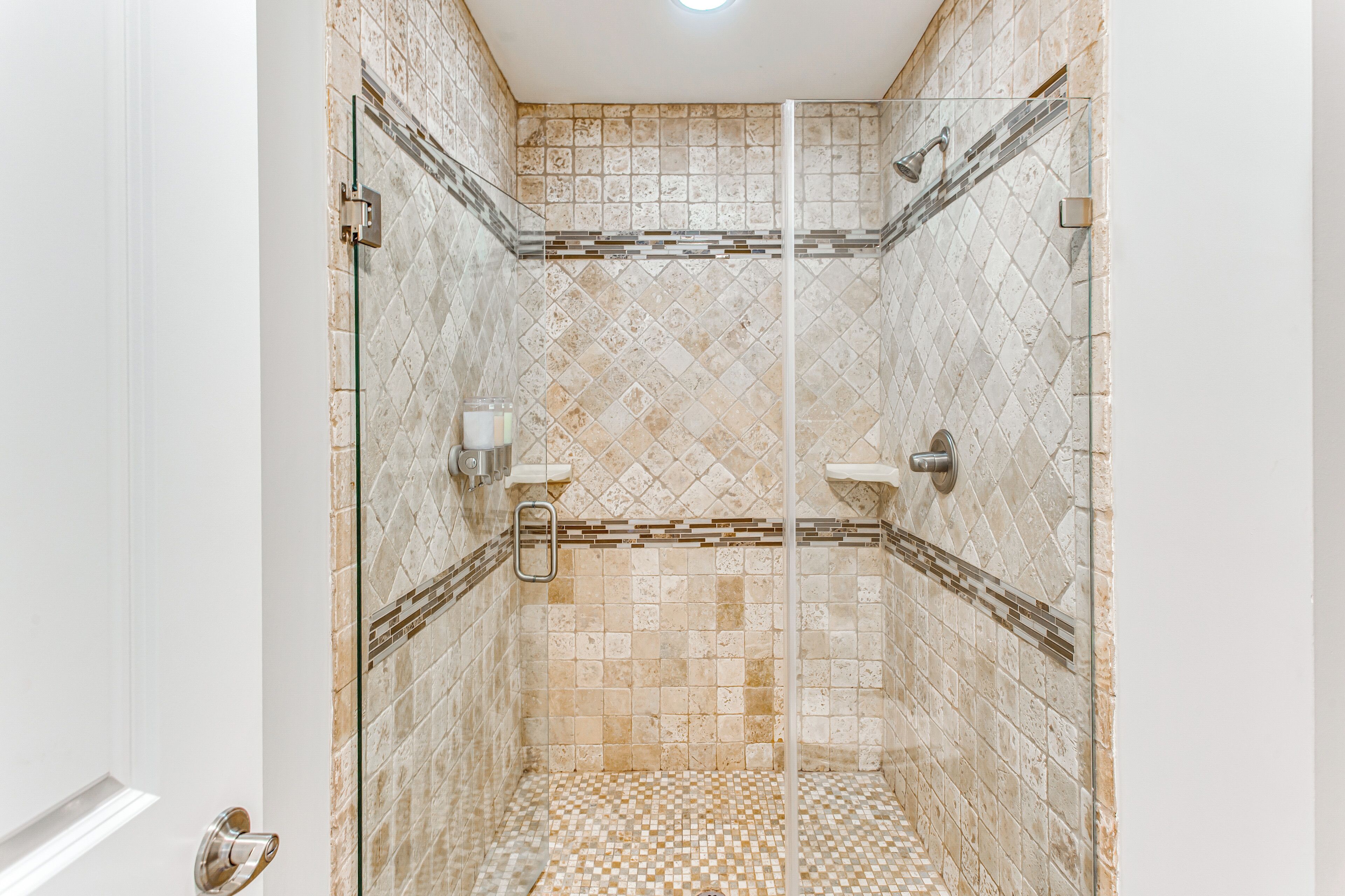 A walk-in shower with a tiled floor and walls, a glass door, and a showerhead.