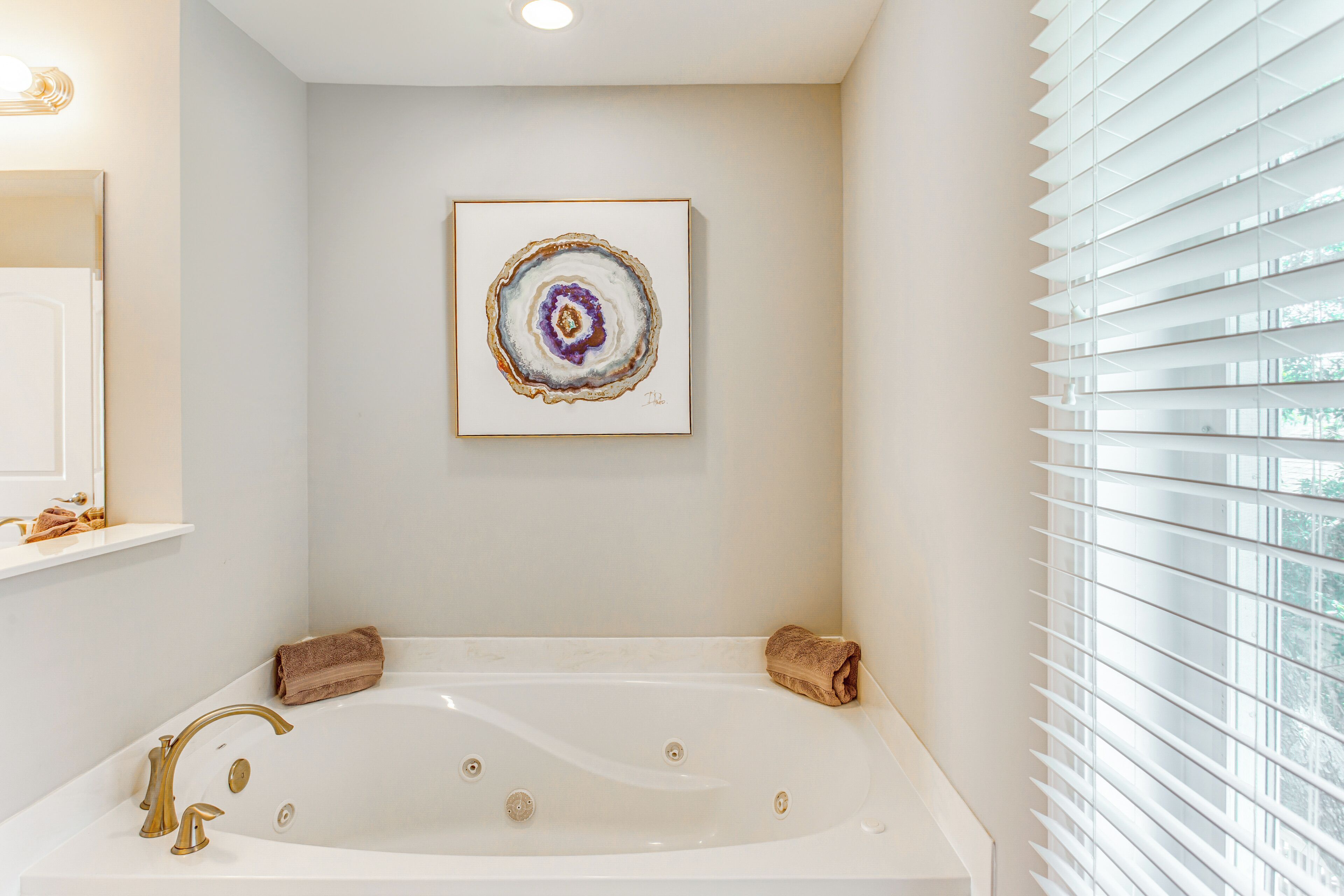 Un bagno moderno con una vasca freestanding, un quadro appeso al muro e una finestra con persiane.