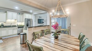 Une cuisine moderne avec des meubles blancs, un réfrigérateur en acier inoxydable et un coin repas comprenant une table en bois et des chaises vertes.