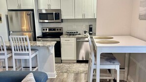 Une cuisine moderne avec des meubles blancs, des appareils en acier inoxydable et un coin repas comprenant une table et des chaises blanches.