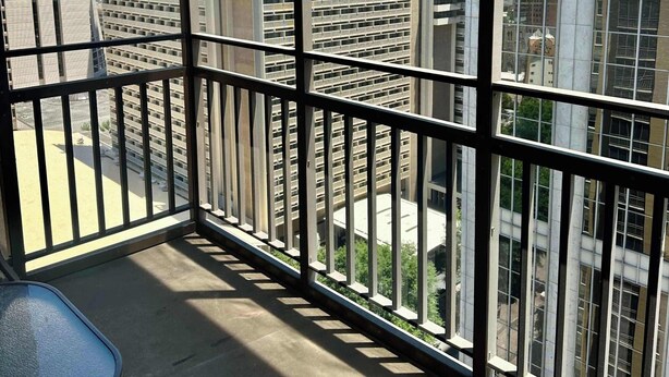 Un balcon offrant une vue sur des immeubles de grande hauteur, dont un bâtiment circulaire remarquable.