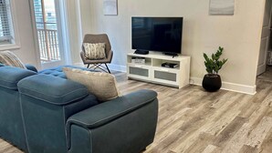Un salon moderne avec un canapé d’angle, un téléviseur à écran plat posé sur un meuble de télévision blanc et une plante en pot.