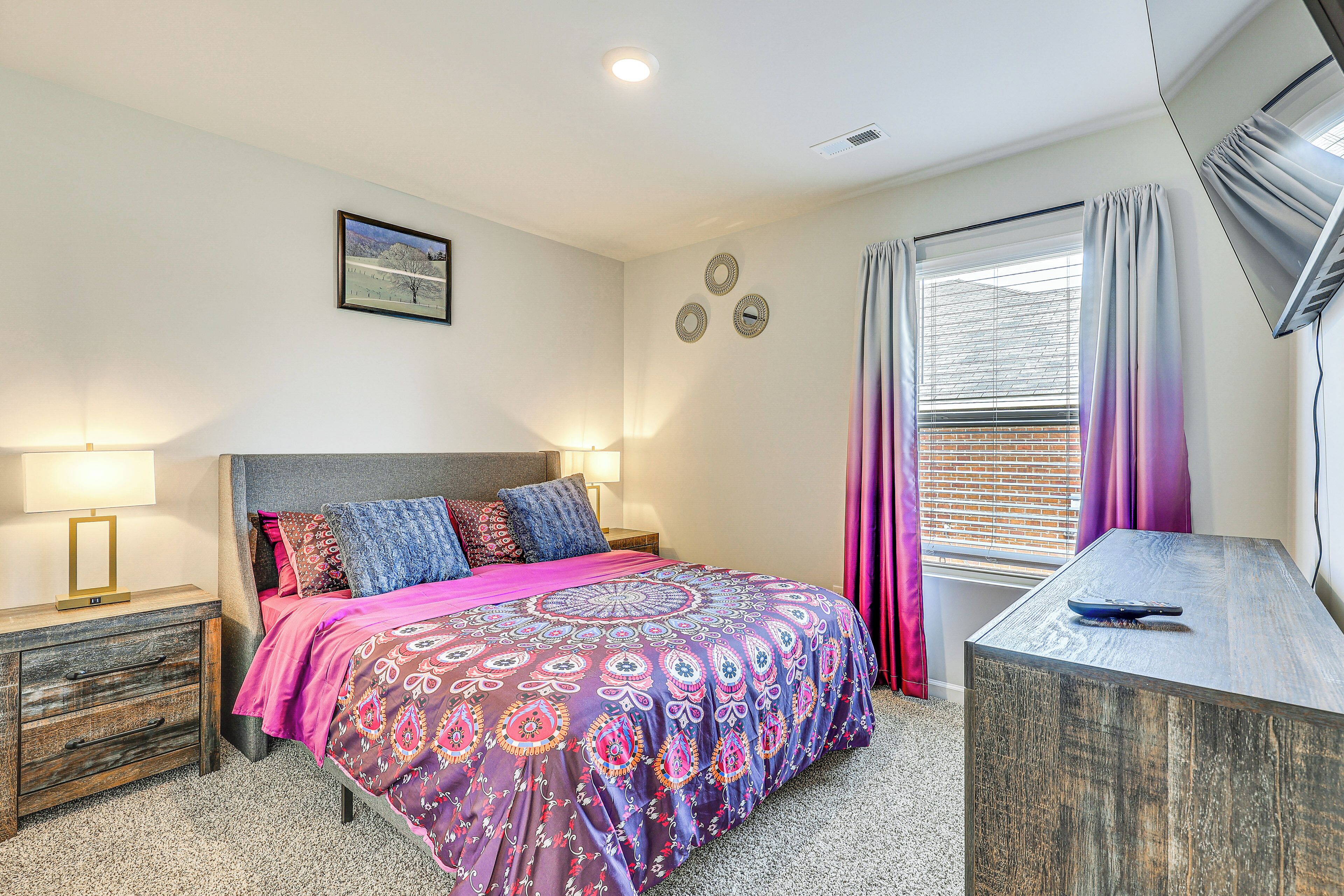 A bedroom with a bed, bedside tables, a dresser, a window with curtains, and wall decor.