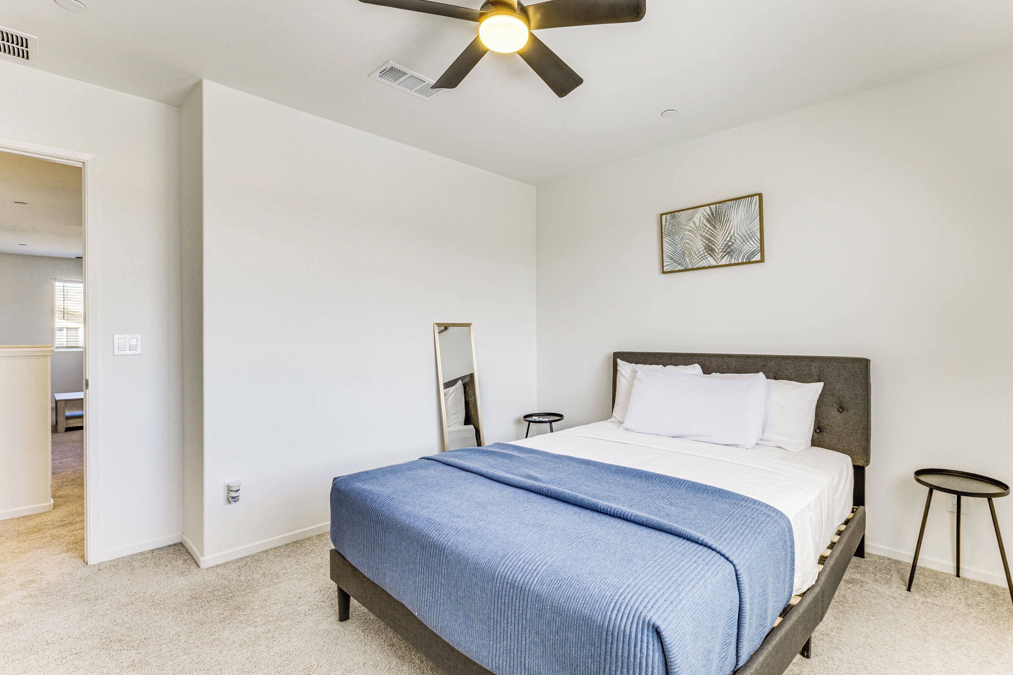 A bedroom with a bed, a ceiling fan, a bedside table, a small round table, and a framed picture on the wall.