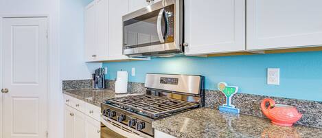Una cocina con gabinetes blancos, un microondas de acero inoxidable, una estufa a gas y encimeras de granito.