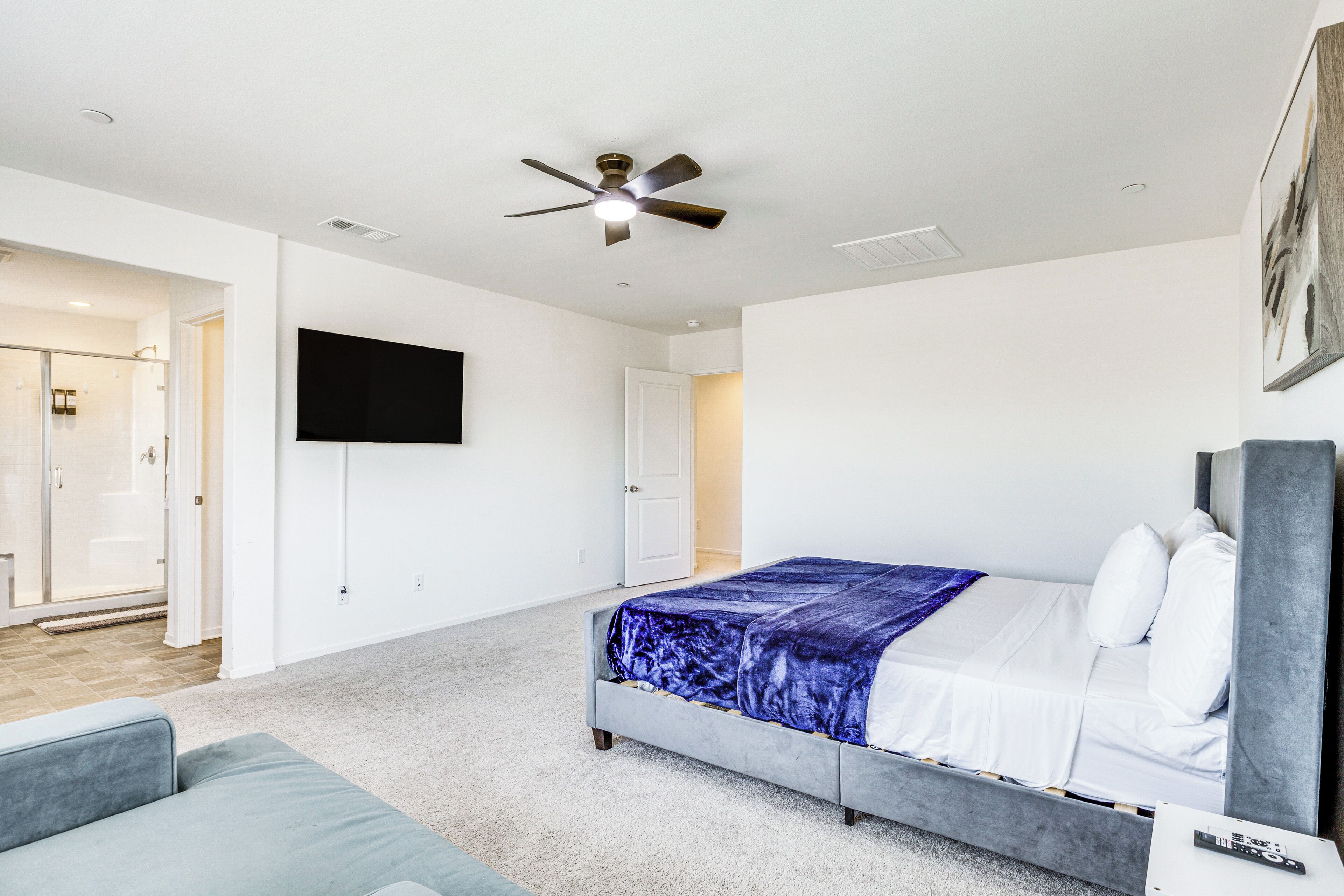 A bedroom with a bed, a ceiling fan, a TV, and a door leading to a bathroom.