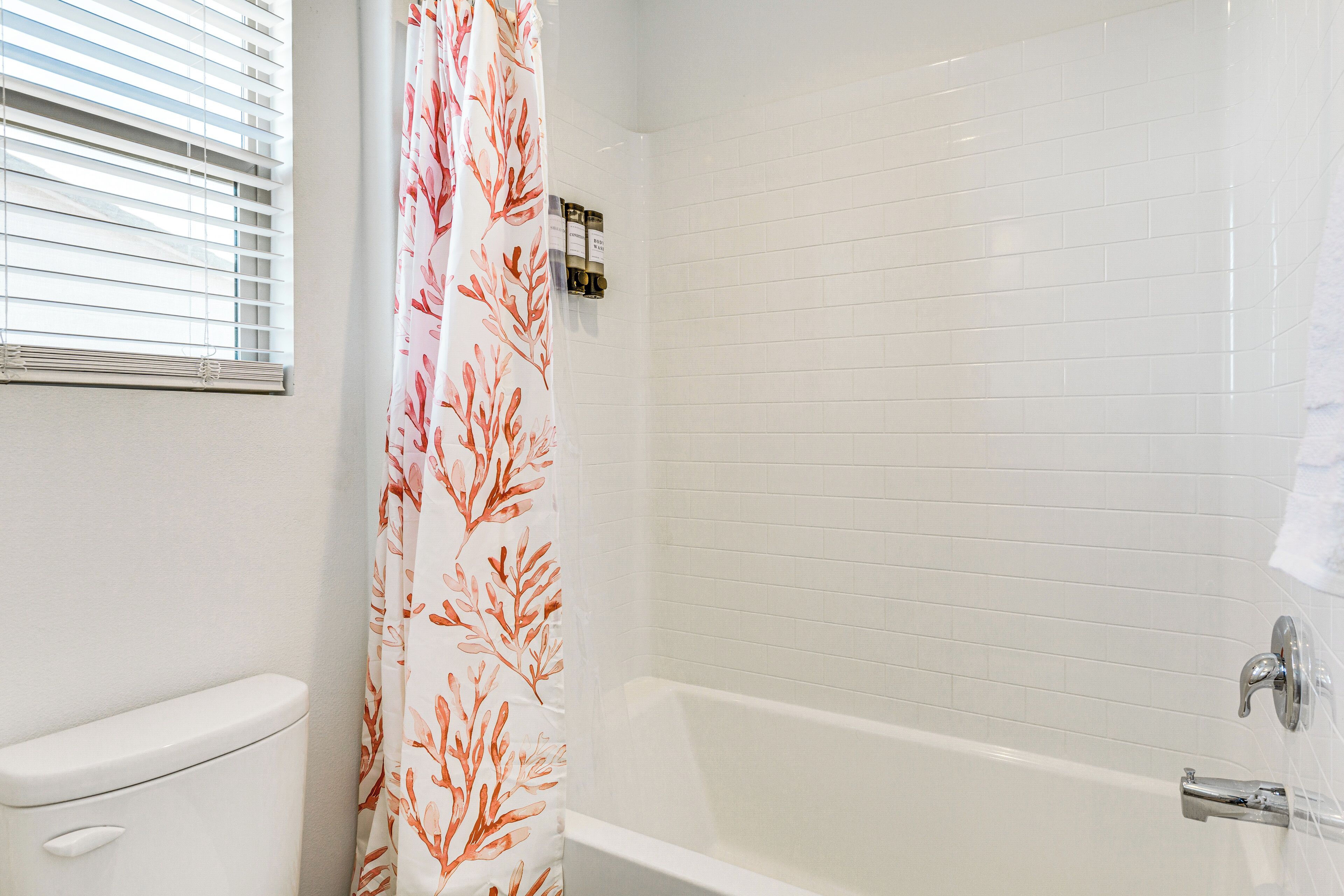 A bathroom with a toilet, a shower curtain with a leaf pattern, and a bathtub with white tiled walls.