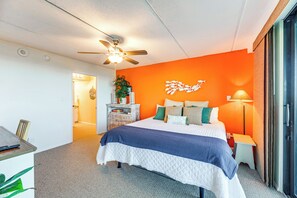A hotel room with a bed, a desk, a ceiling fan, and a nightstand with a lamp. - Beachfront Views: Breezy Port Aransas Condo! (Port Aransas)