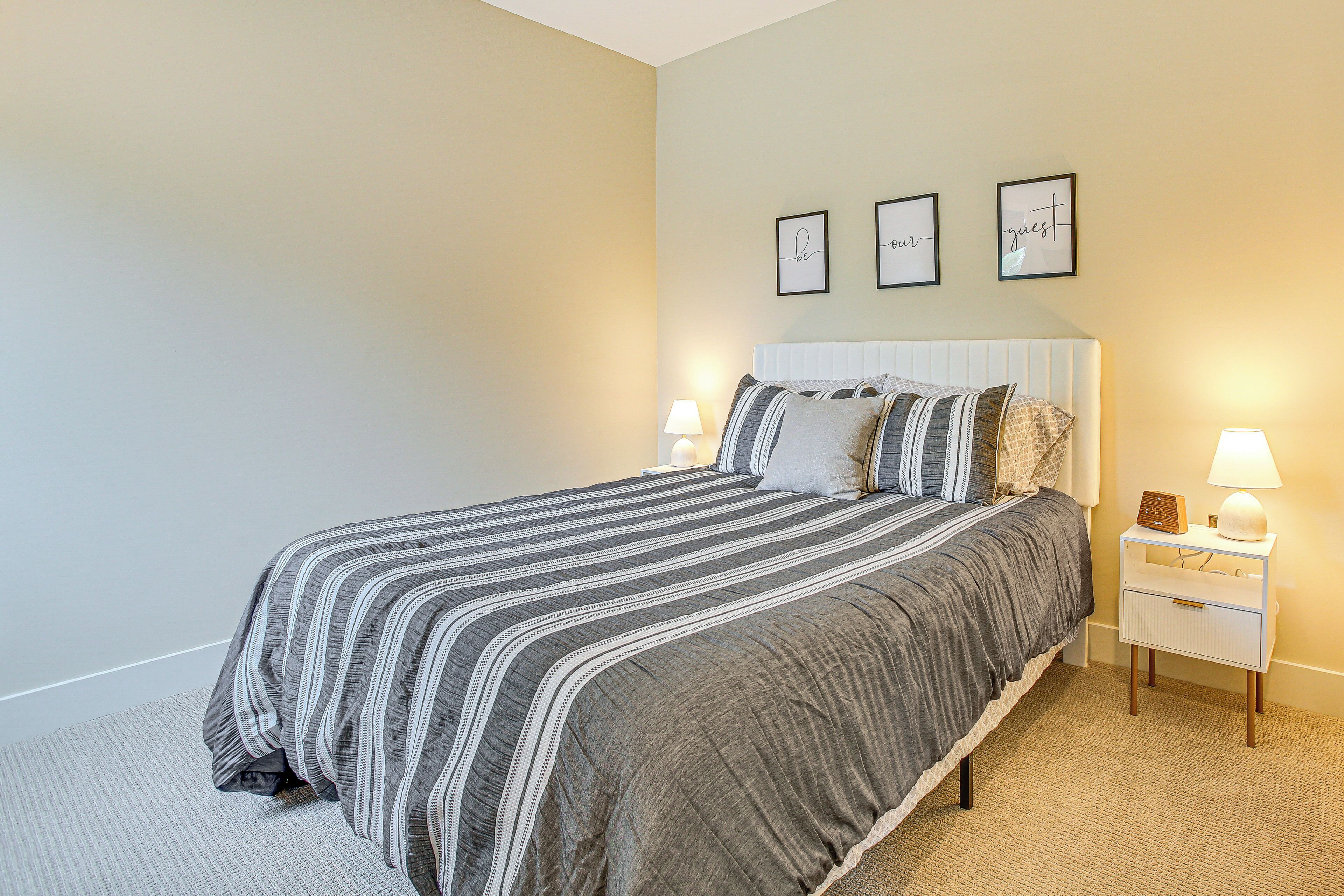 A neatly made bed with striped bedding, a bedside table with a lamp, and three framed pictures on the wall.