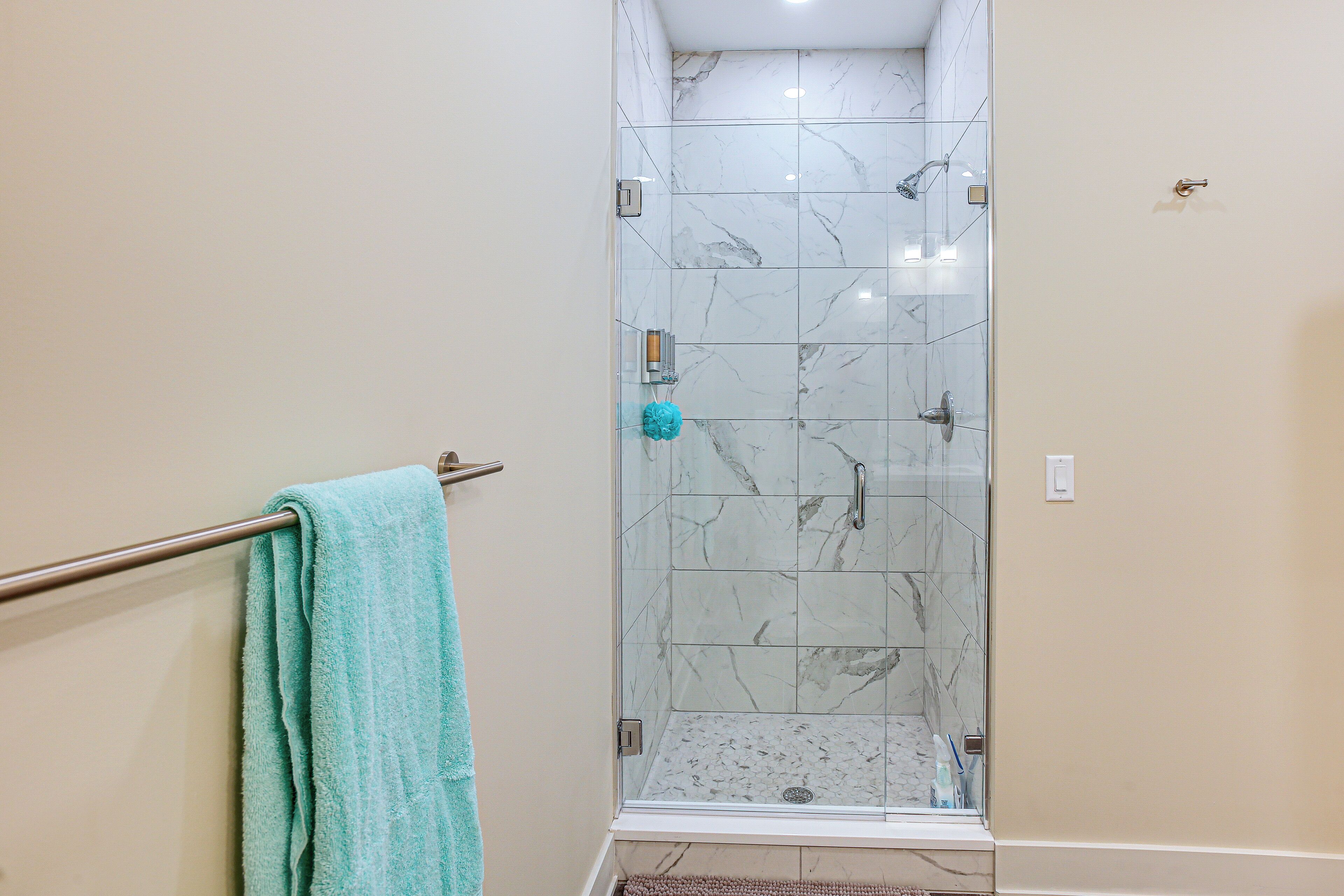 A glass-enclosed shower with marble tiles, a towel rack with a towel, and a light switch on the wall.