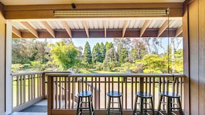 Un balcon doté d’une balustrade en bois, de trois tabourets de bar noirs et offrant une vue sur un jardin avec différents arbres et arbustes.